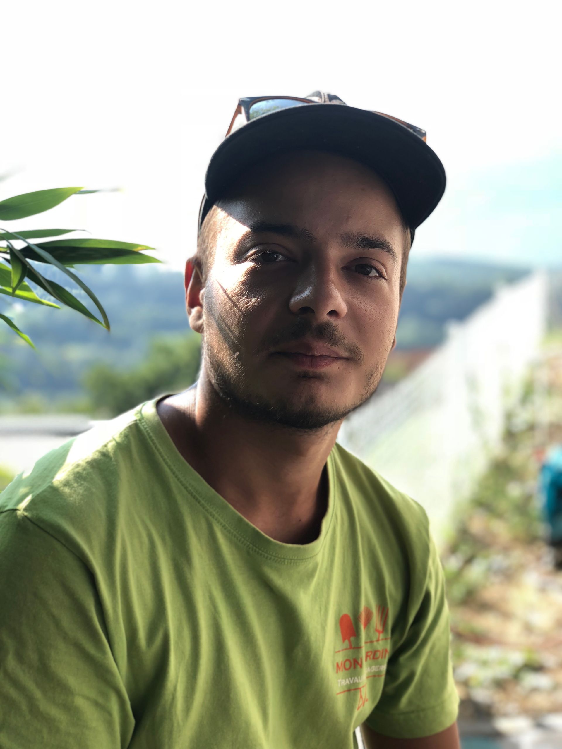 Un homme portant une chemise verte et un chapeau noir regarde la caméra.