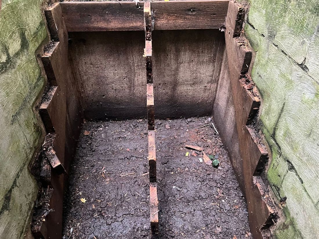 Narrow rusty metal chute or shaft with concrete walls and a dark, empty bottom.