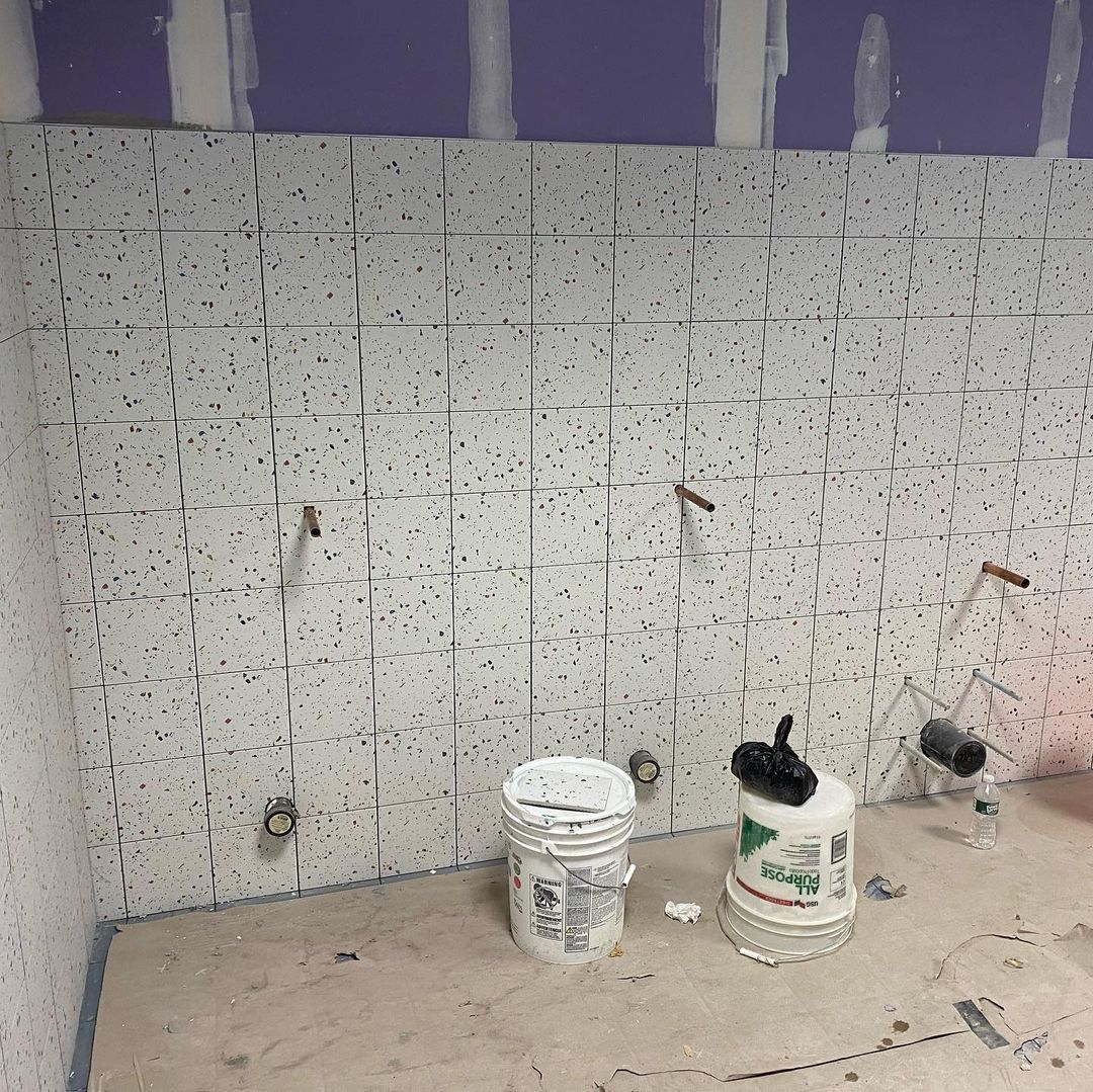 Two buckets of paint are sitting on the floor in front of a tiled wall.