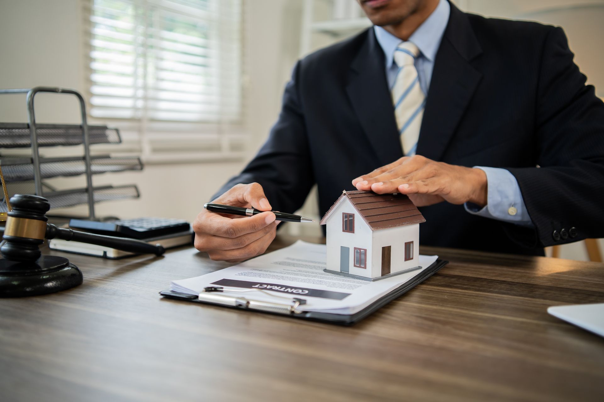 Hands shielding a model house over a signed contract, representing estate planning protection