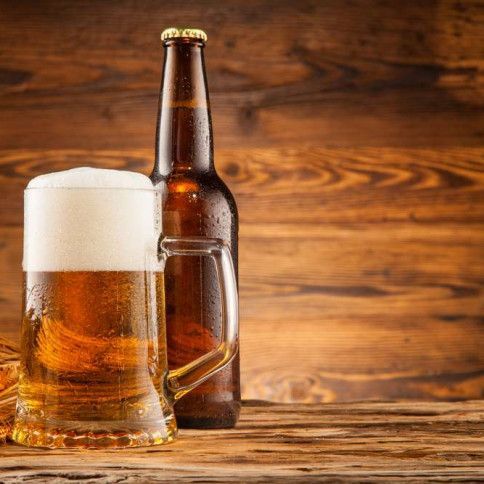 A bottle of beer and a glass of beer are on a wooden table.