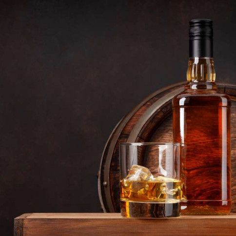 A bottle of whiskey and a glass of whiskey with ice on a wooden table.