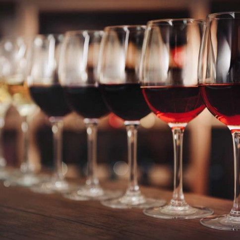 A row of wine glasses filled with red wine on a wooden table.