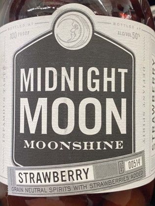 A bottle of midnight moon strawberry moonshine is sitting on a table.