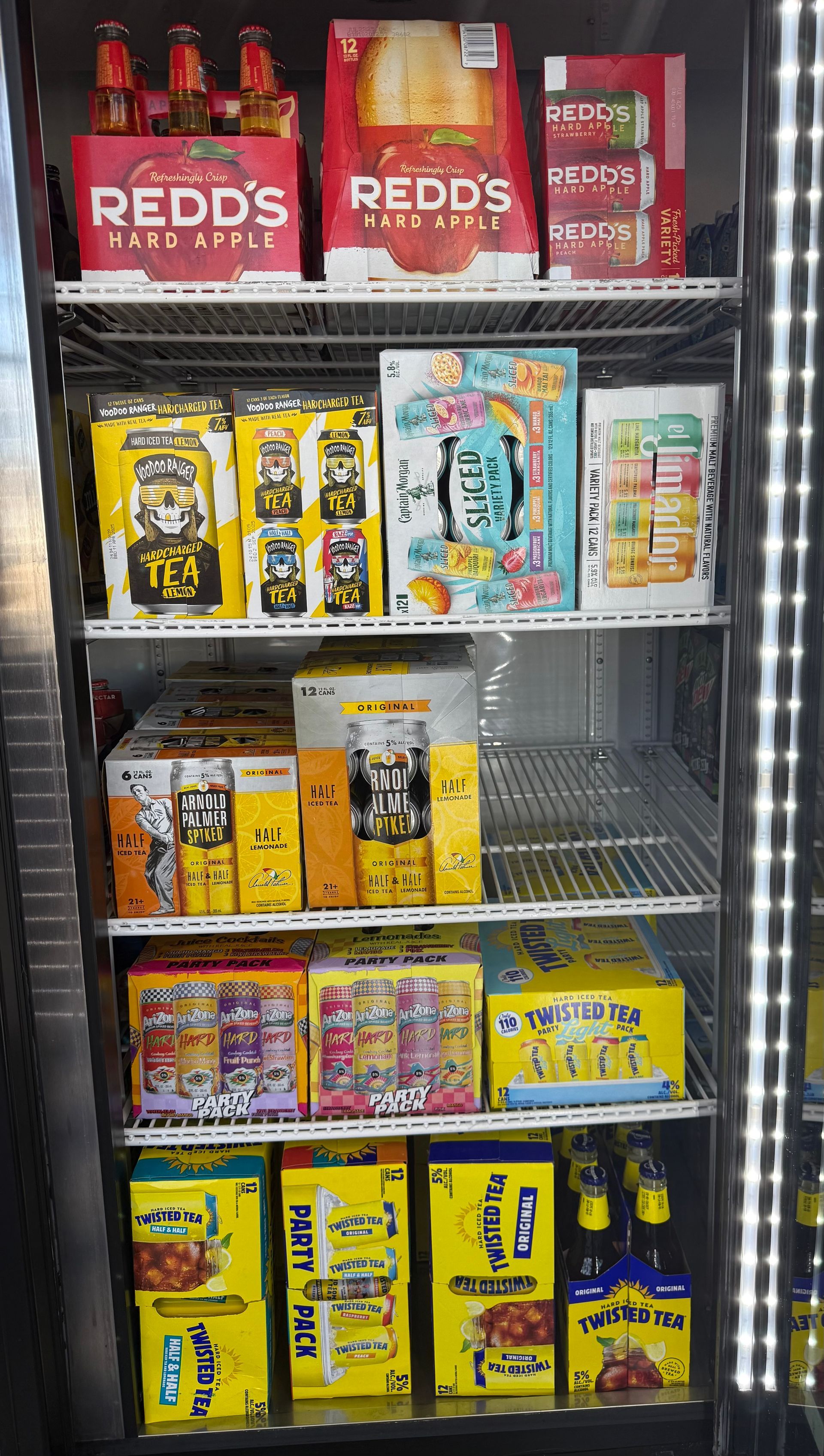 A refrigerated display case filled with various alcoholic beverages, including Redd's and other fruity drinks.