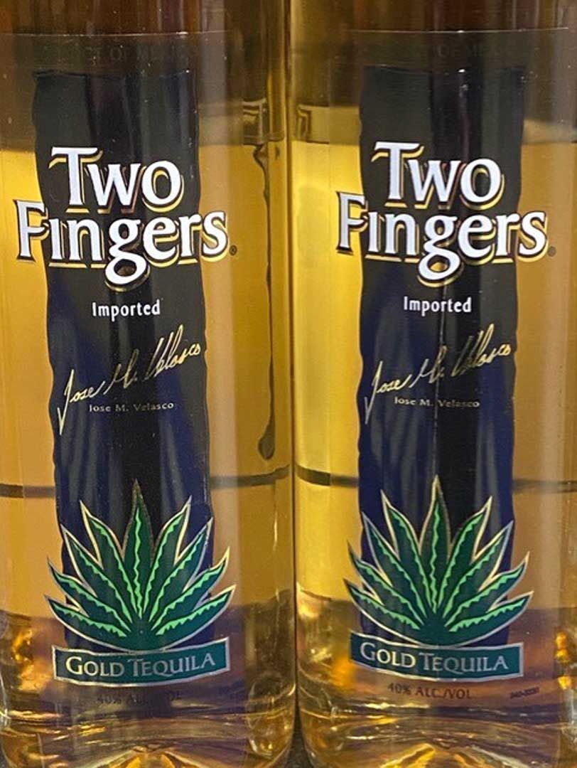 Two bottles of two fingers gold tequila are sitting next to each other.
