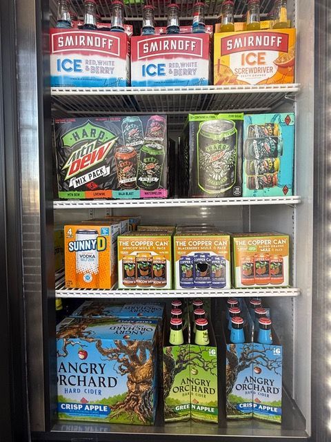 A refrigerator filled with alcoholic beverages, including Smirnoff Ice, hard seltzer, and Angry Orchard cider.