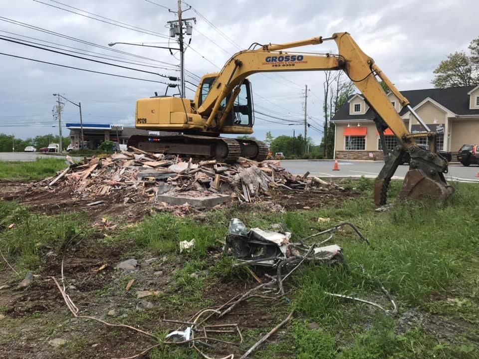 A yellow excavator is destroying a building in a field.