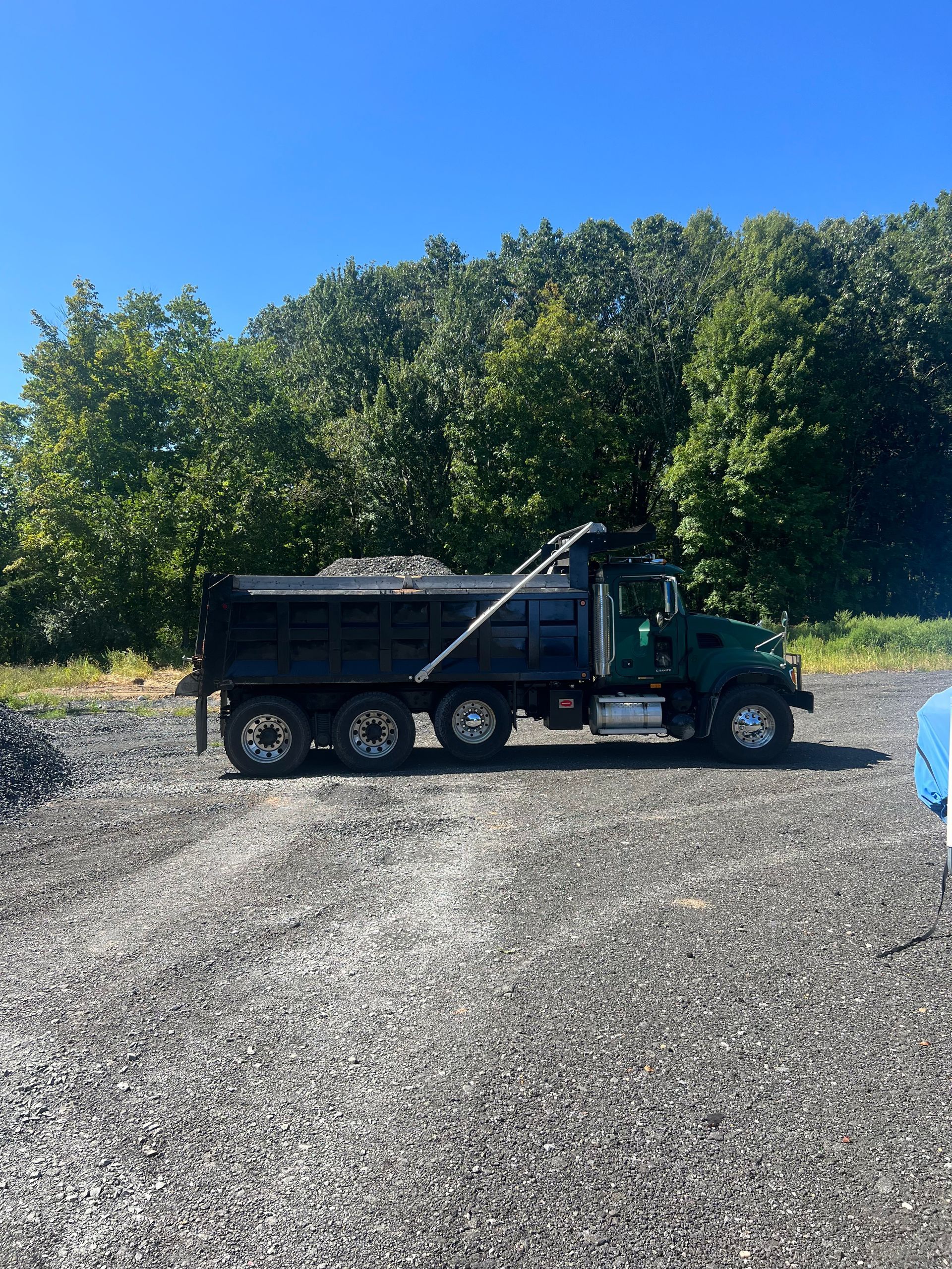 A dump truck is parked in a gravel lot with trees in the background.