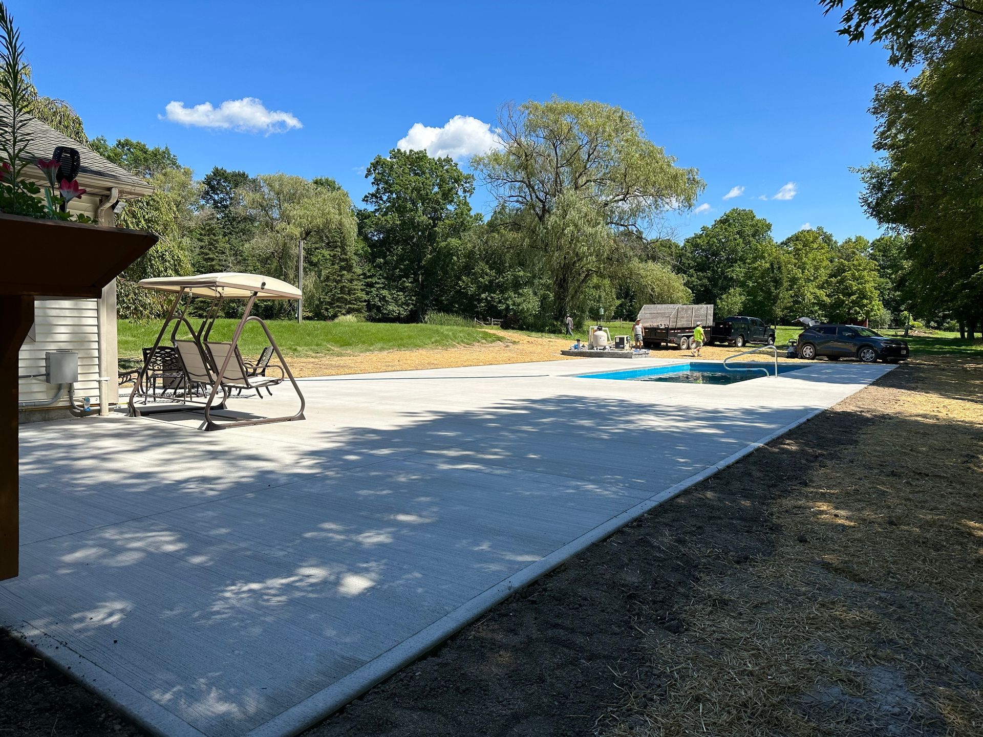 A patio with a swing and a swimming pool in the background