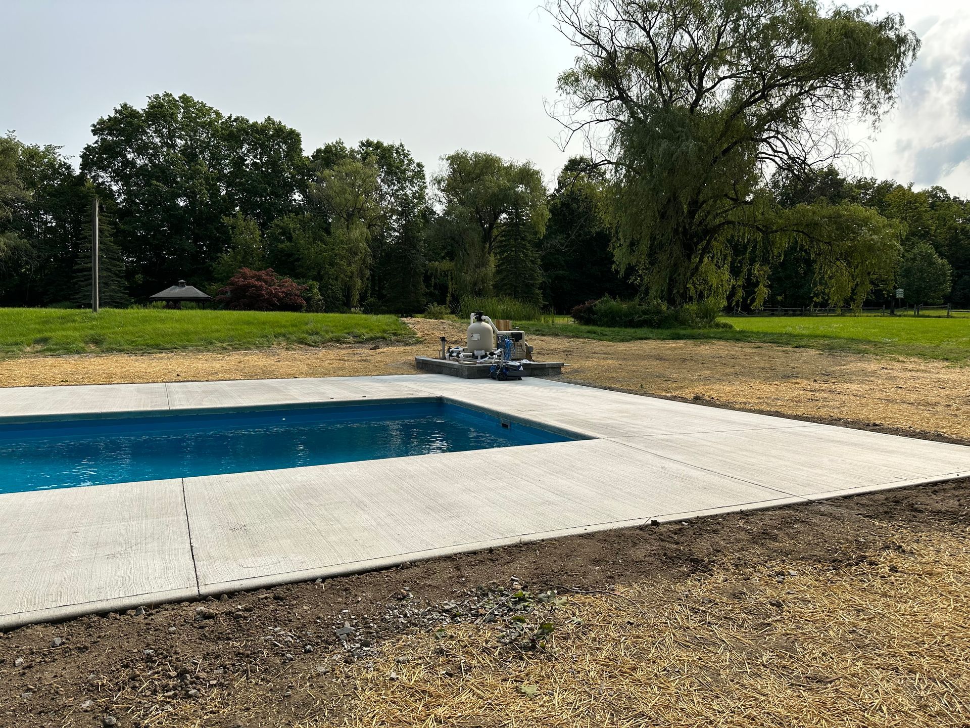 A large swimming pool is in the middle of a field surrounded by trees.