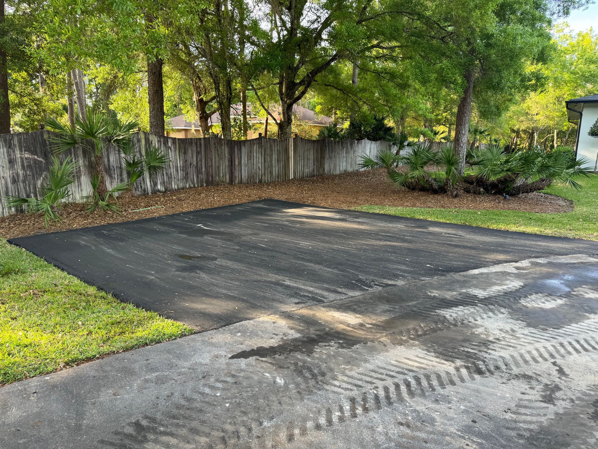 A driveway with a fence and trees in the background.