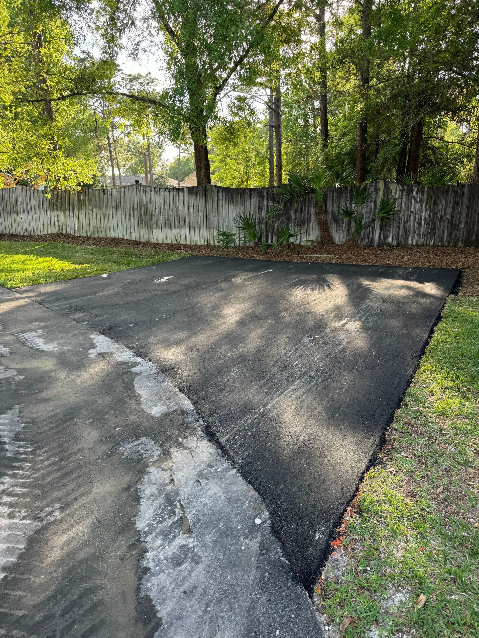 A driveway with a fence and trees in the background.