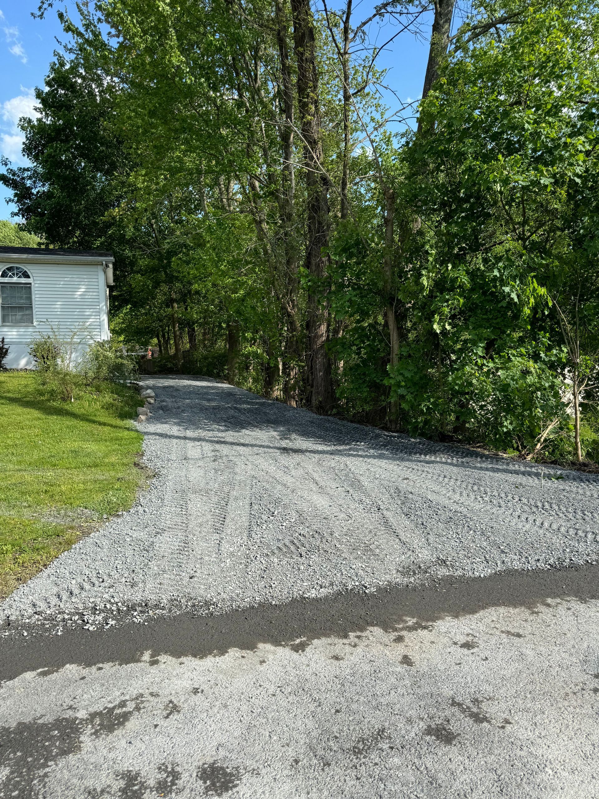 A gravel driveway leading to a house in the woods.