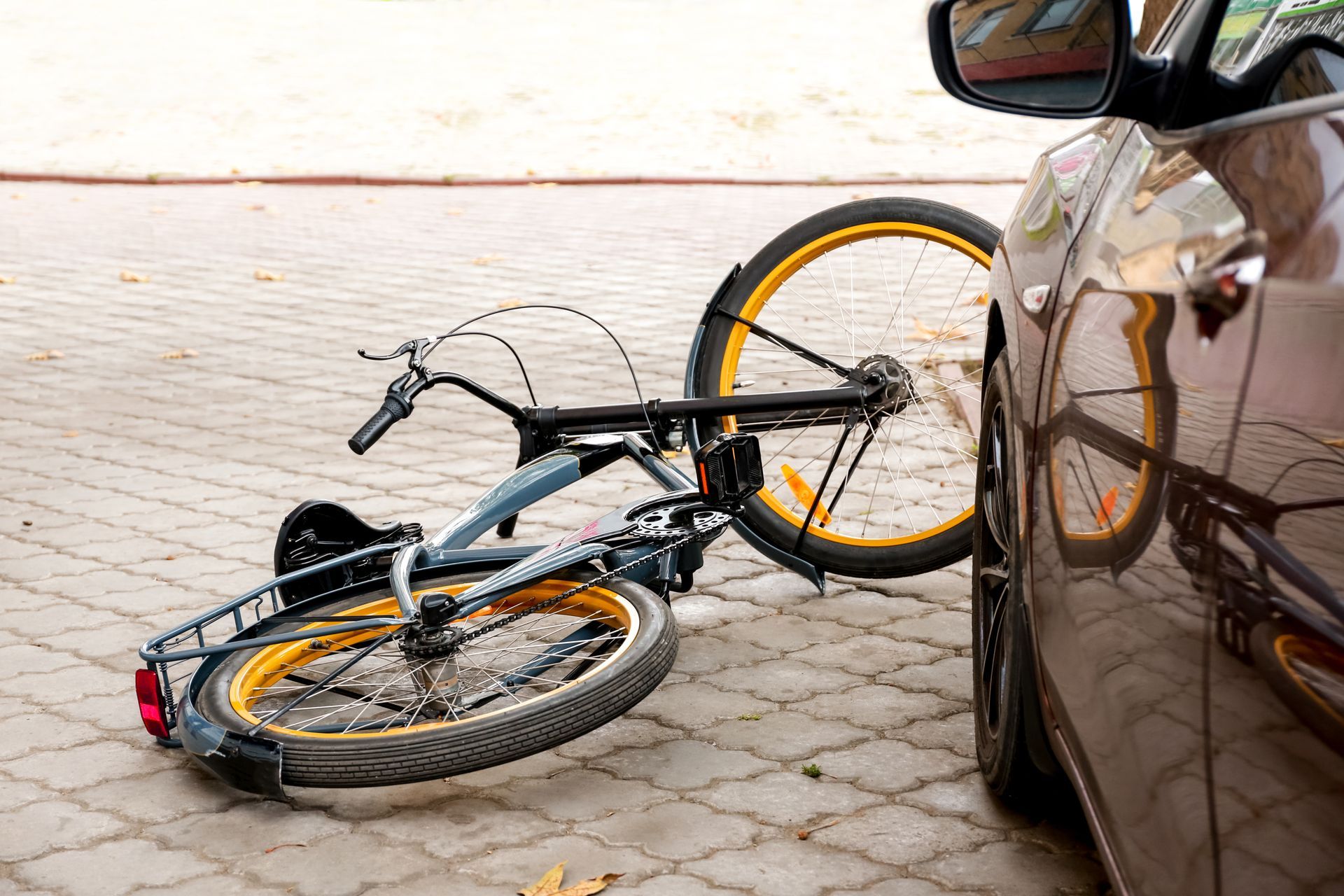 Bike lying on pavement next to a car, possibly after a collision.