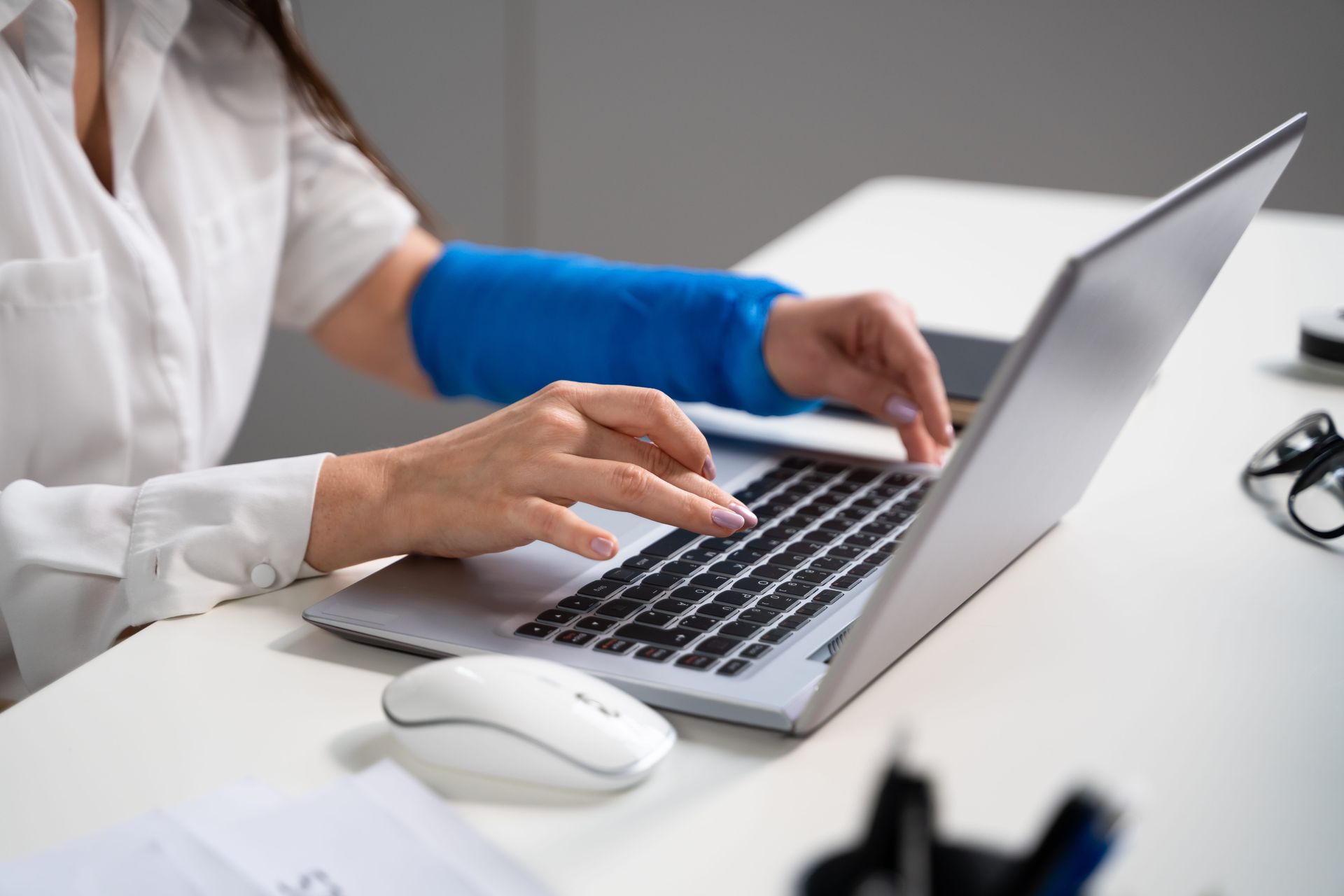 Person typing on a laptop at a desk beside a white mouse, wearing blue gloves