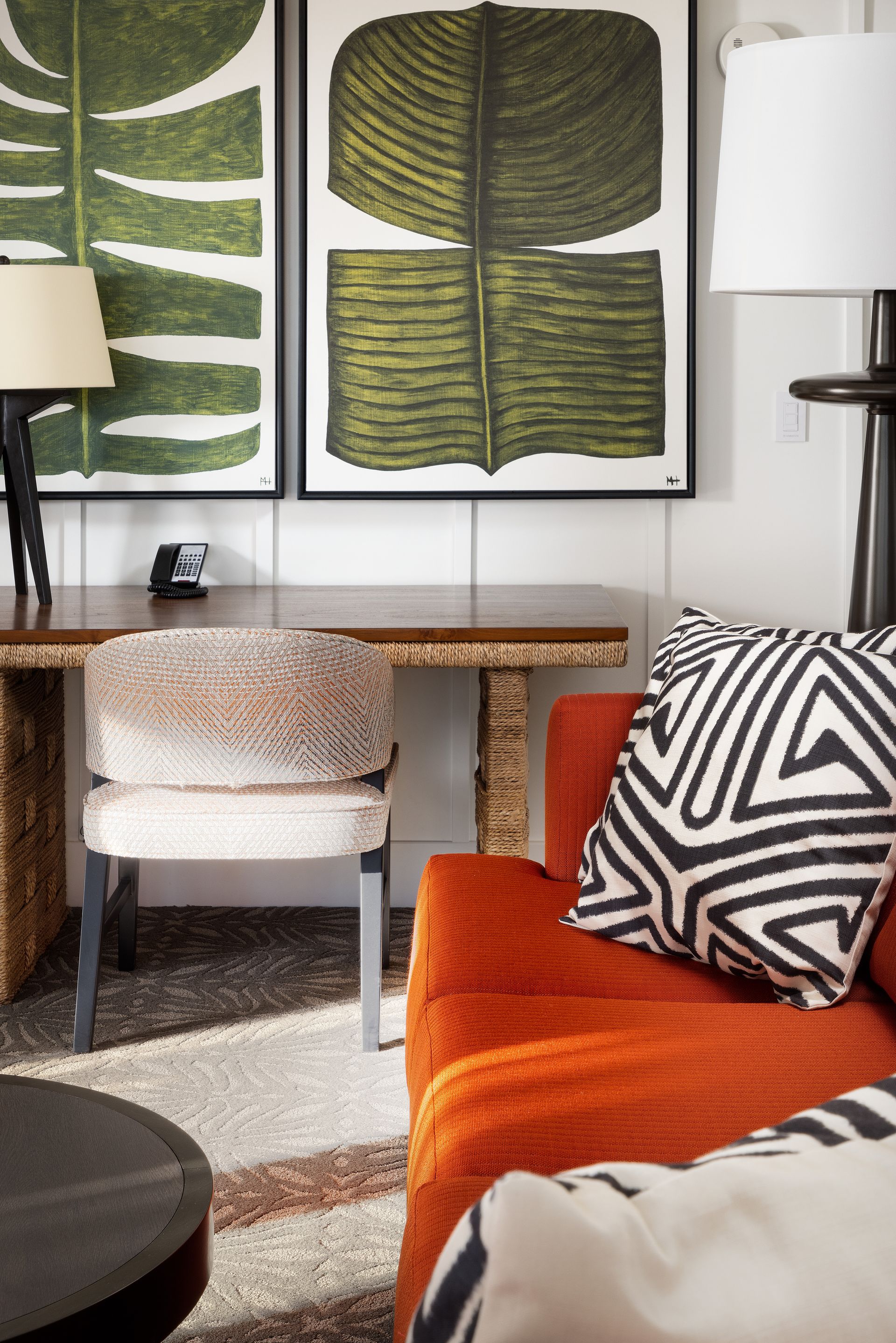 A living room with a couch , chair , desk and paintings on the wall.