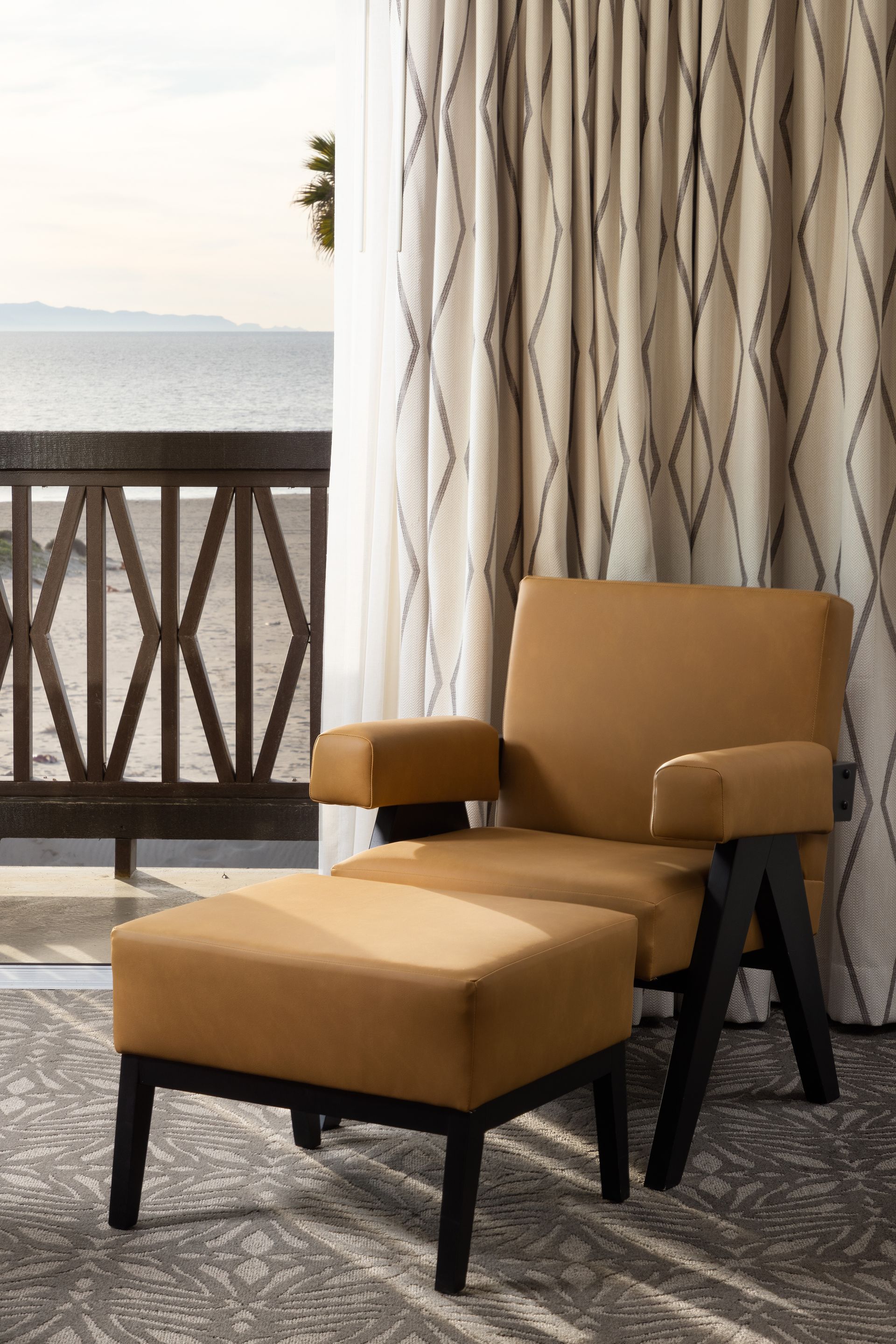 A chair and ottoman in a hotel room with a view of the ocean.