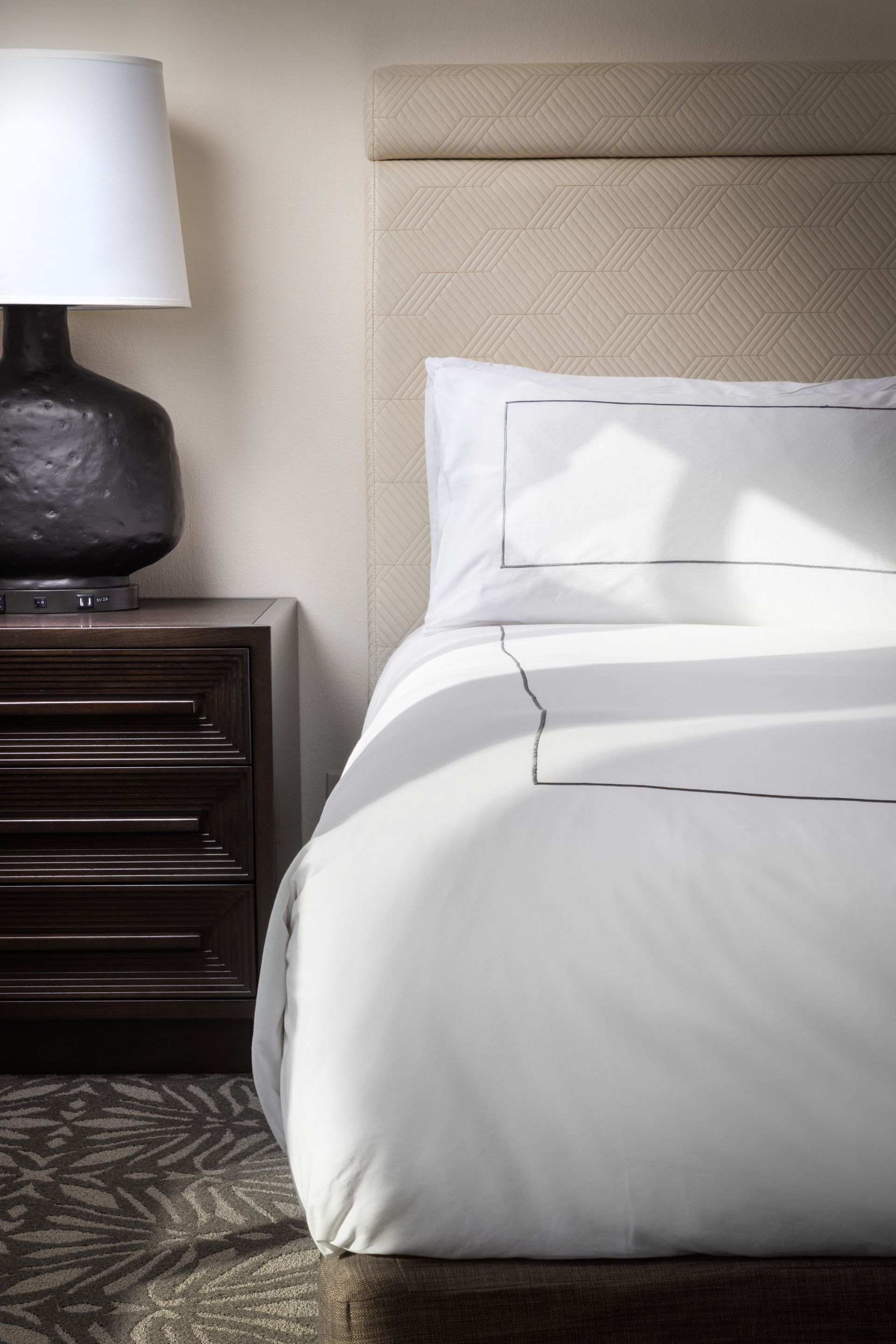 A hotel room with a bed , nightstand and lamp