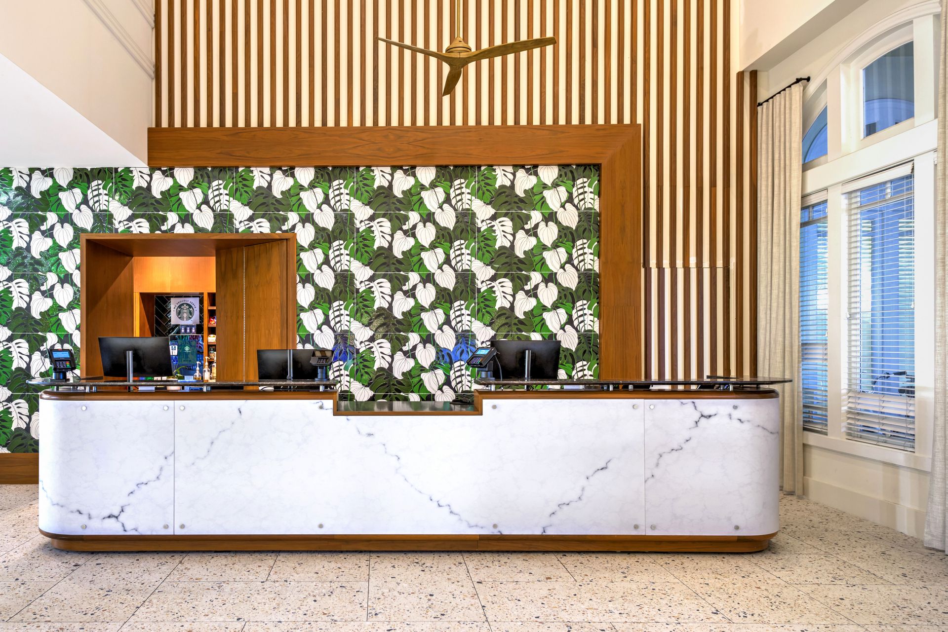 A hotel lobby with a long white counter and a ceiling fan.
