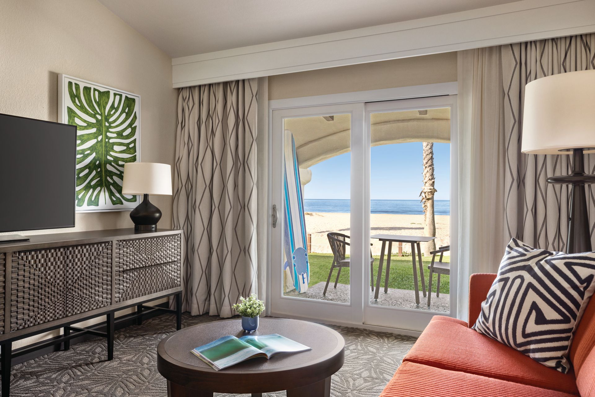 A living room with a couch , table , television and sliding glass doors leading to the beach.