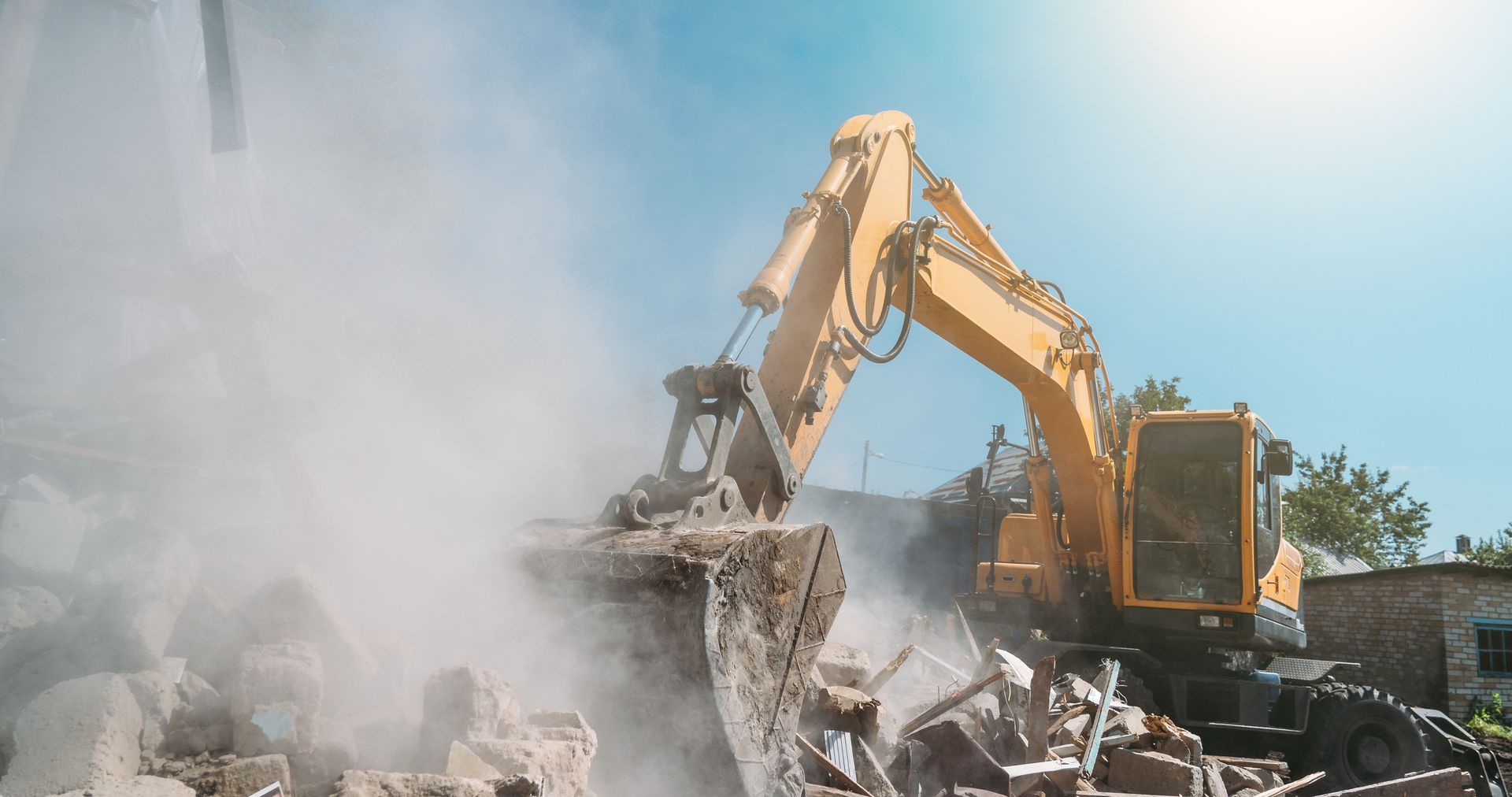 A yellow excavator is demolishing a building with smoke coming out of it.