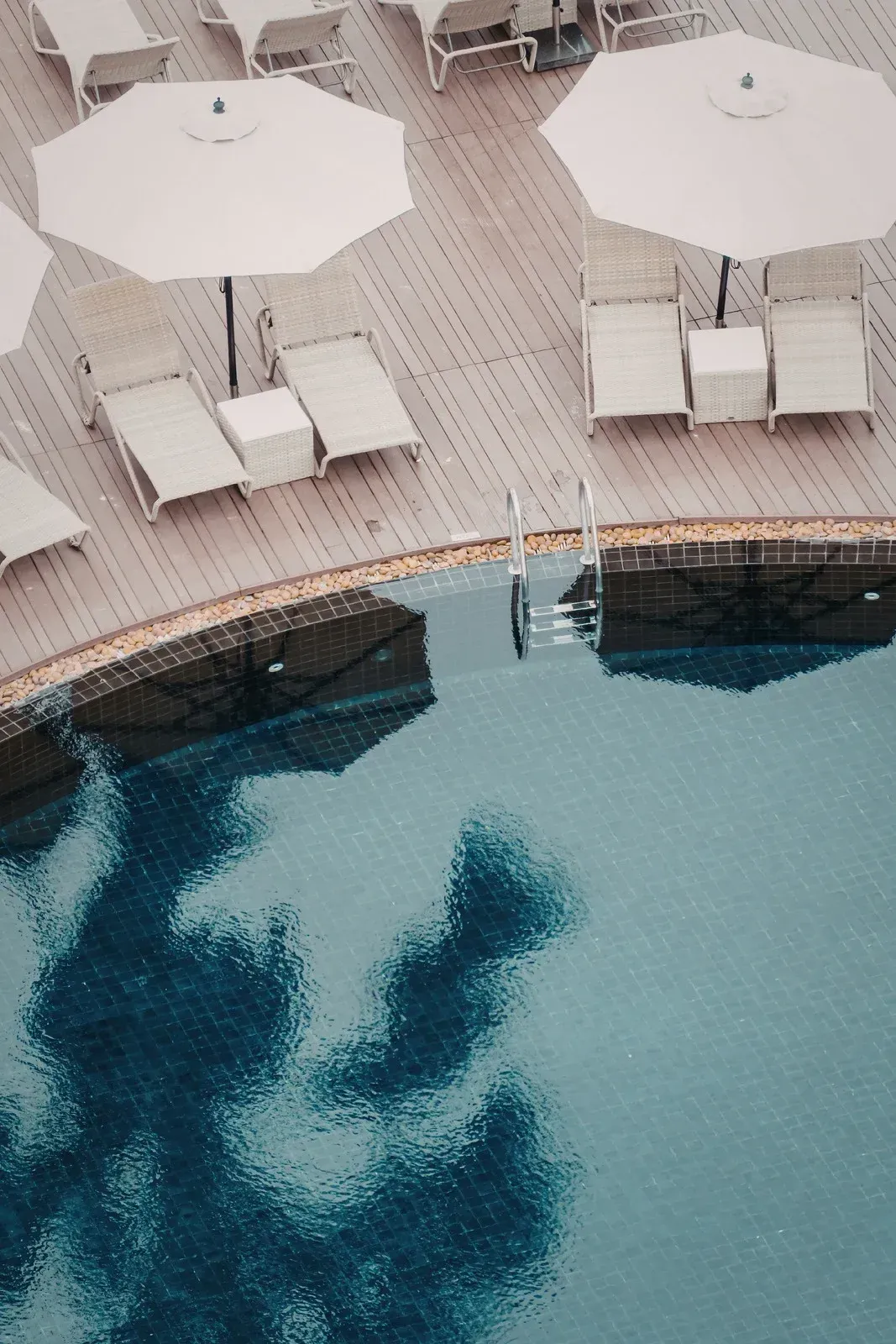 High-angle view of a swimming pool with lounge chairs and white umbrellas arranged on the surrounding wooden deck.