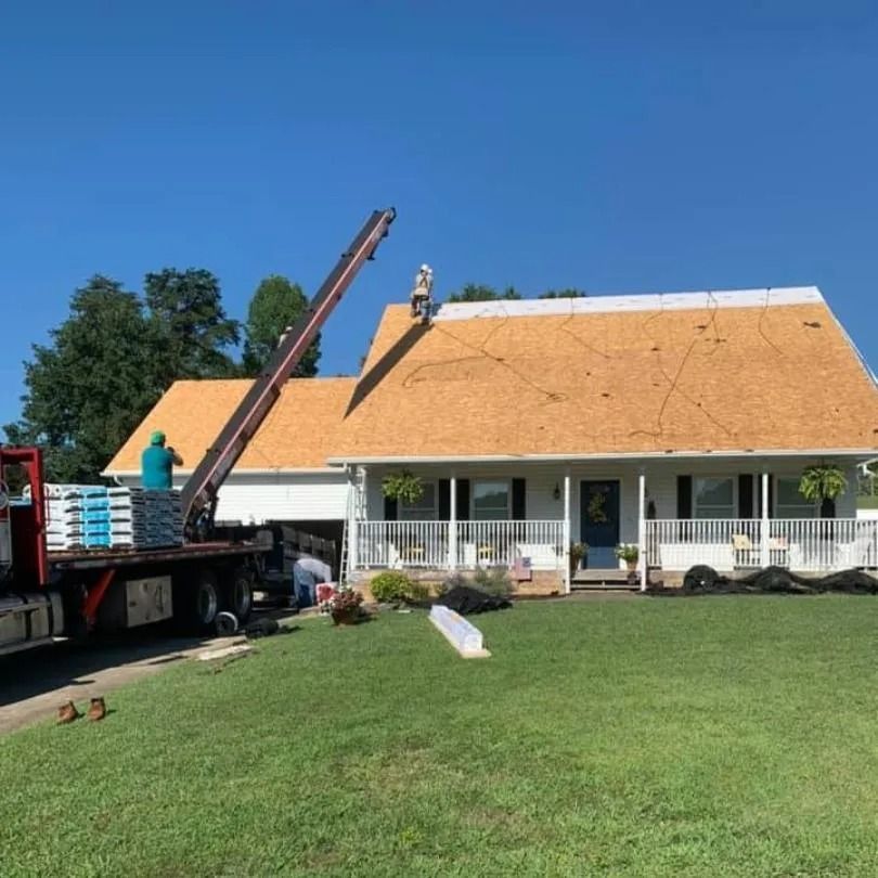 Workers use a crane to lift building materials onto the roof of a house under construction on a sunny day.