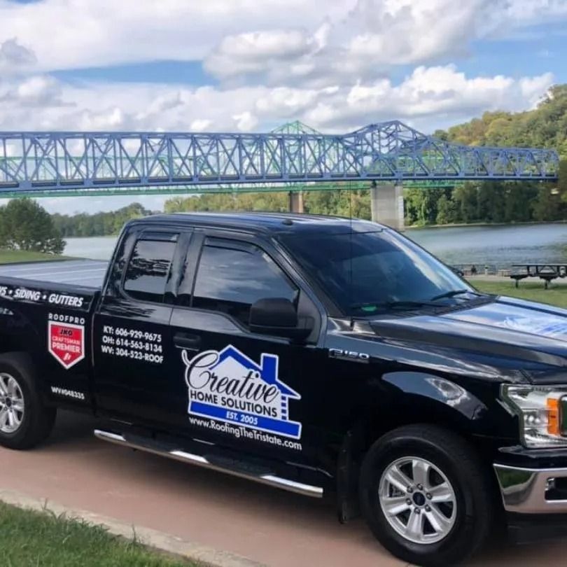 A black pickup truck for Creative Home Solutions parked outdoors with a large blue truss bridge in the background.