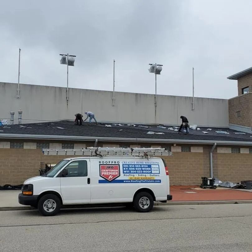 Three workers repair a dark shingled roof while a white 