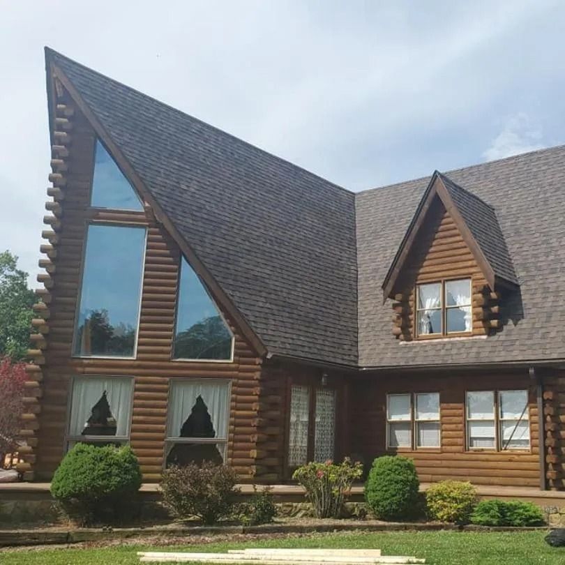 A large log cabin house featuring a tall triangular window section and a gabled dormer under a dark shingled roof.