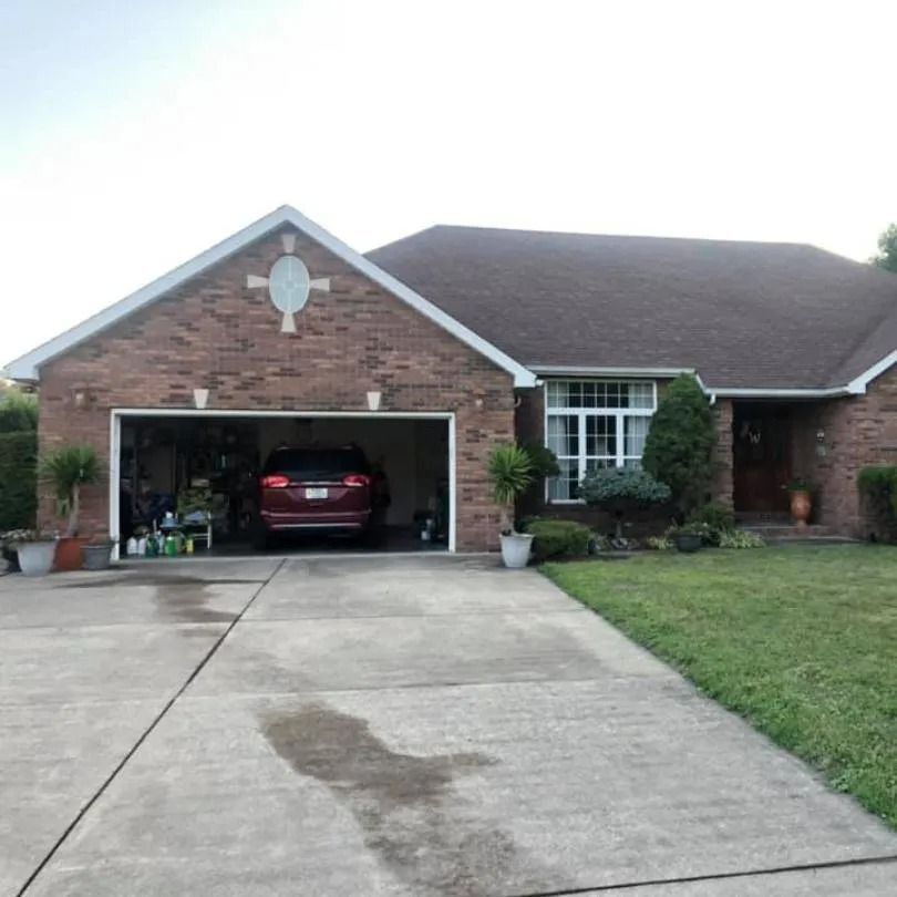 A brick, single-story house with an attached garage, a parked vehicle, a driveway, and a front lawn.