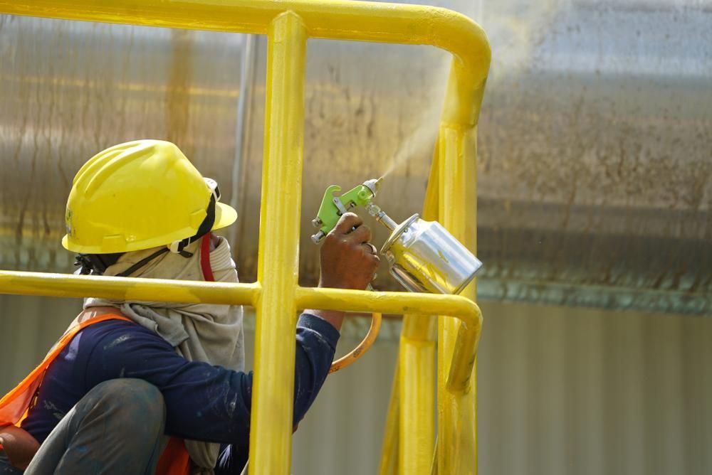 A Man Wearing a Hard Hat is Spraying Paint on a Railing — Cutting Edge Painting Contractors QLD in Veteran, QLD