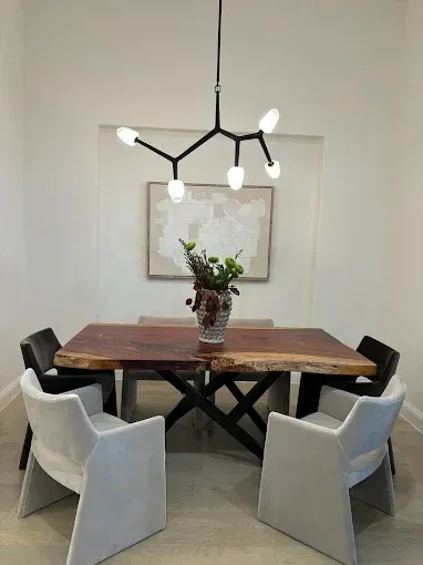 A modern dining room with a live-edge wooden table, four light gray chairs, and a black branching chandelier above.