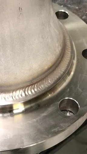 Close-up of a high-quality circular weld connecting a cylindrical pipe to a metal flange with bolt holes.