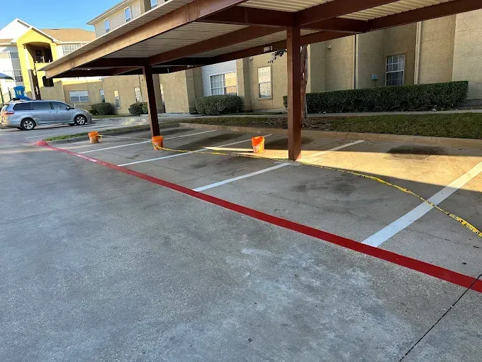 A row of covered parking spaces with painted red and white lines and several small orange traffic cones on the concrete.
