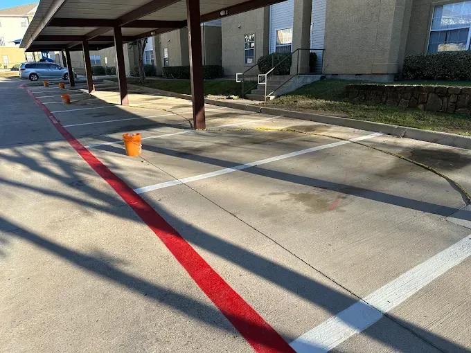 Covered parking area with freshly painted red and white stripes on the concrete, marked by several orange traffic cones.