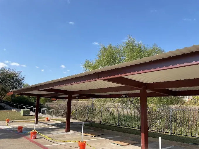 A brown metal carport structure stands over marked parking spaces with orange cones and yellow caution tape.