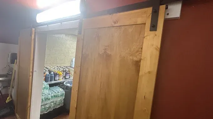 A wooden barn-style sliding door partially open to a back-of-house storage area with shelves and supplies.