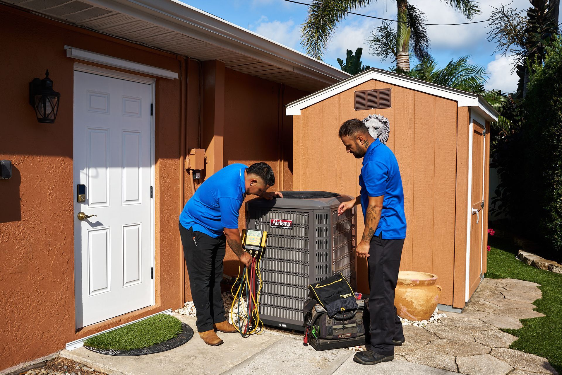 Two teal air conditioning units beside a house on a concrete pad near stone siding