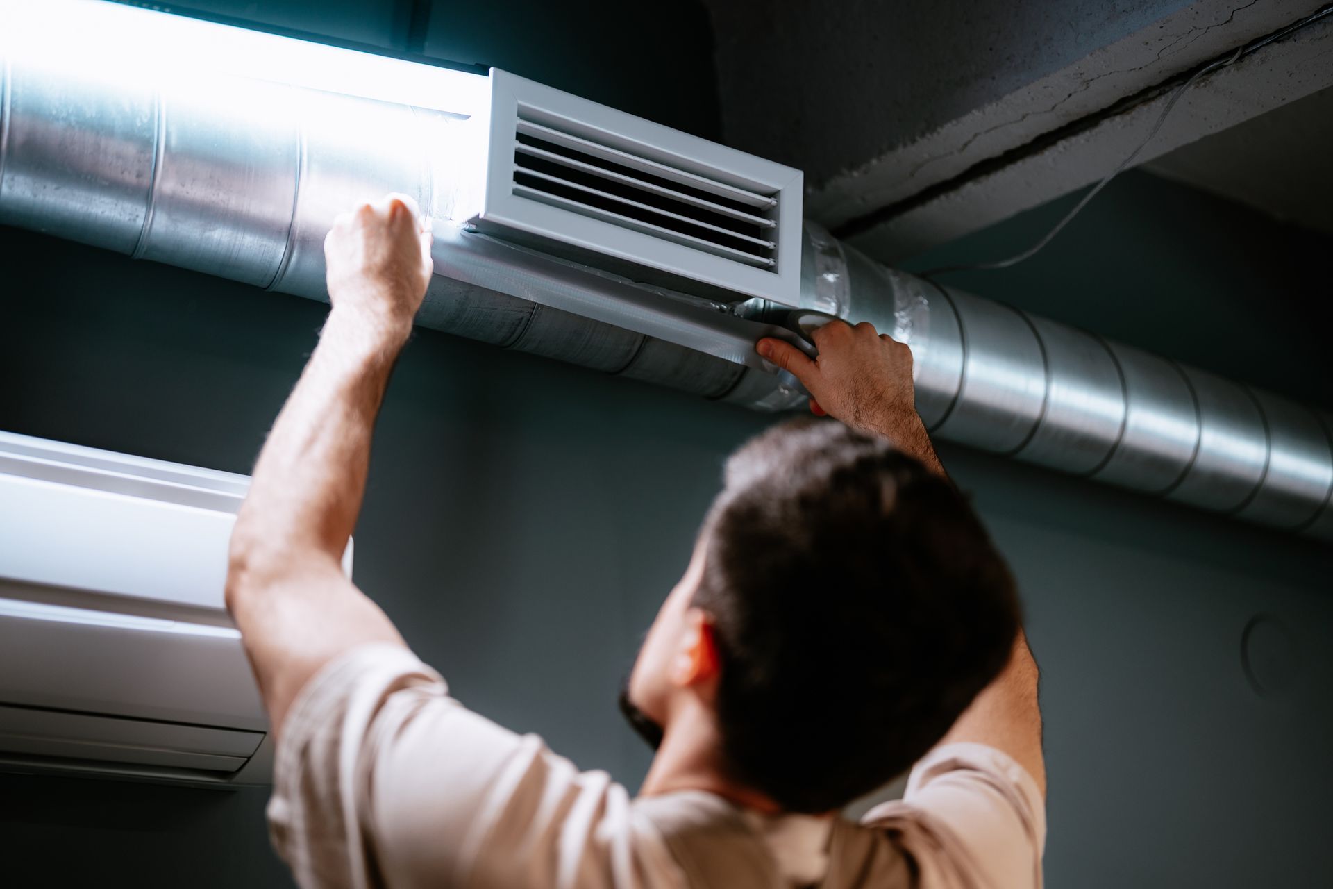 Technician installing a silver HVAC duct in a ceiling space