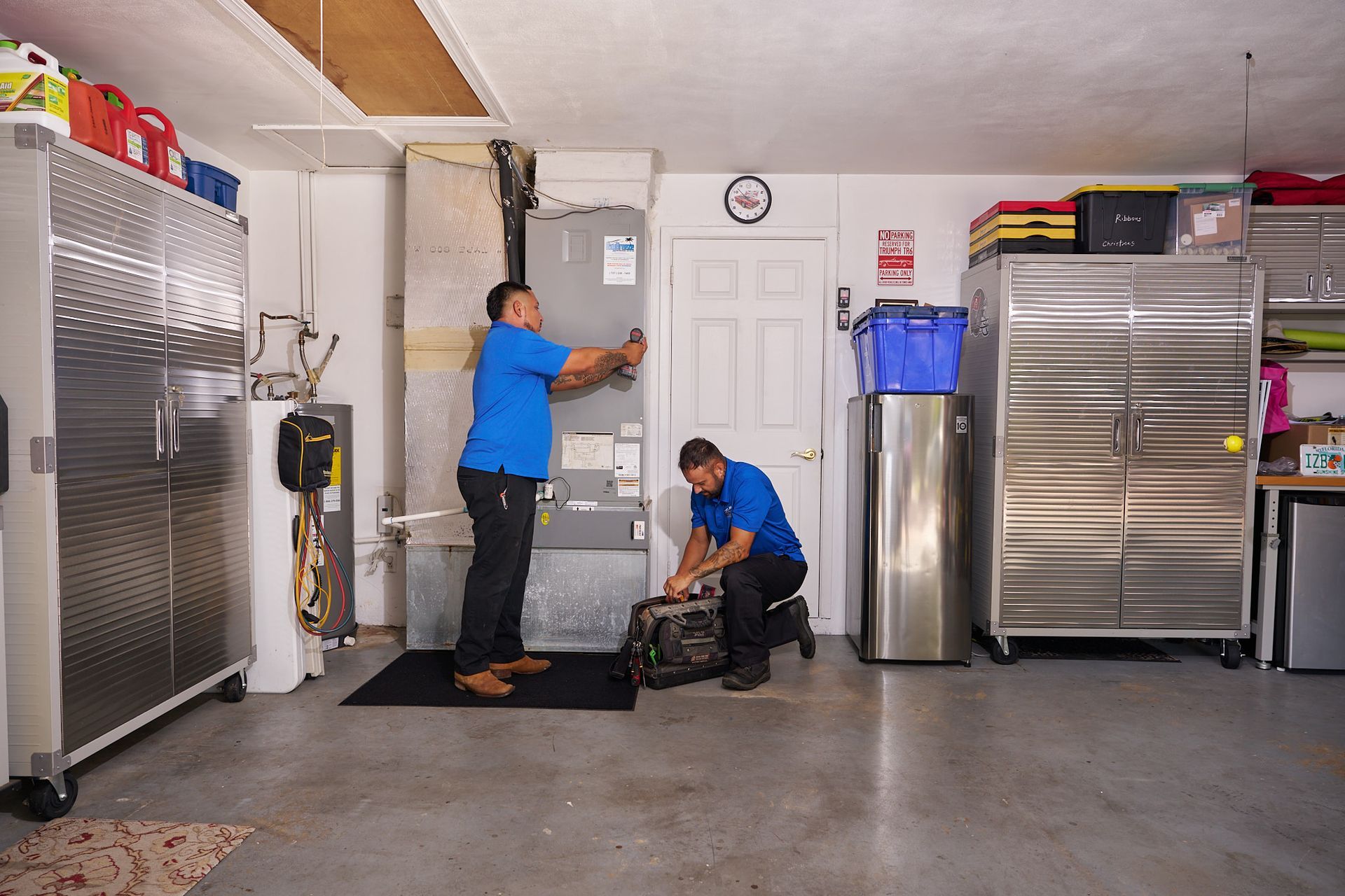 Technician in blue shirt working on a home HVAC unit with tools inside a utility room