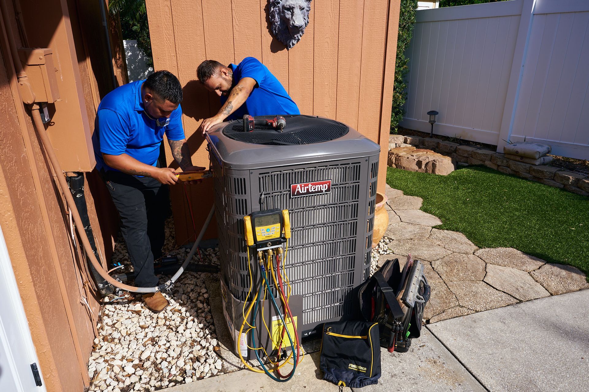 Technician testing HVAC unit outdoors with a multimeter and hoses