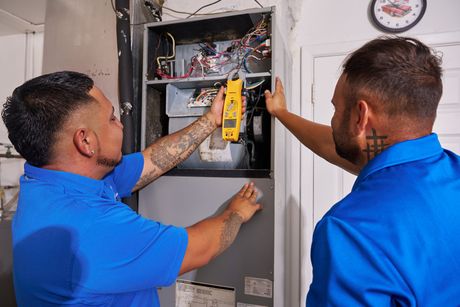 Technician inspecting a furnace unit with a tool in a utility room