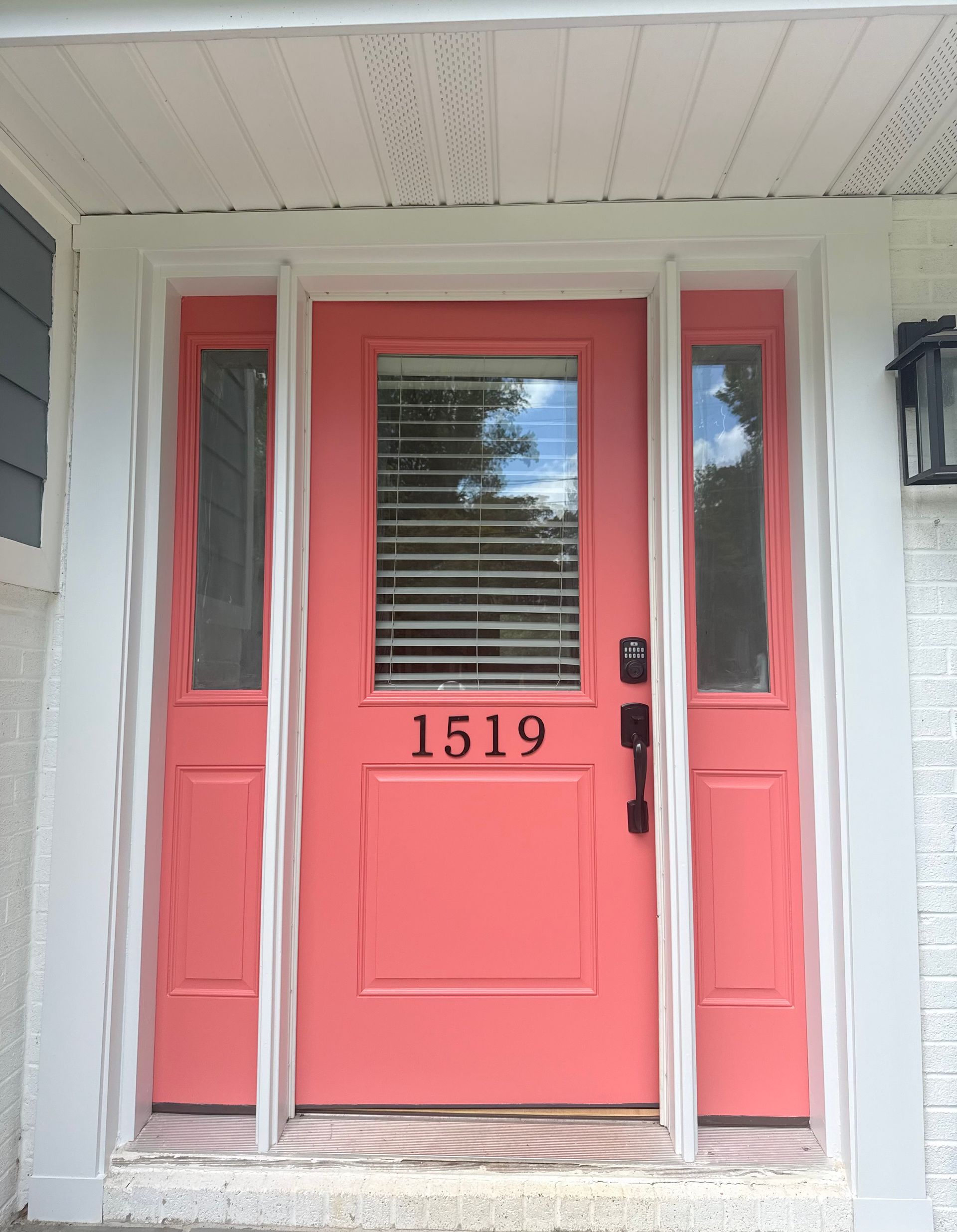 Coral front door with sidelights and house number 1519 under a porch.