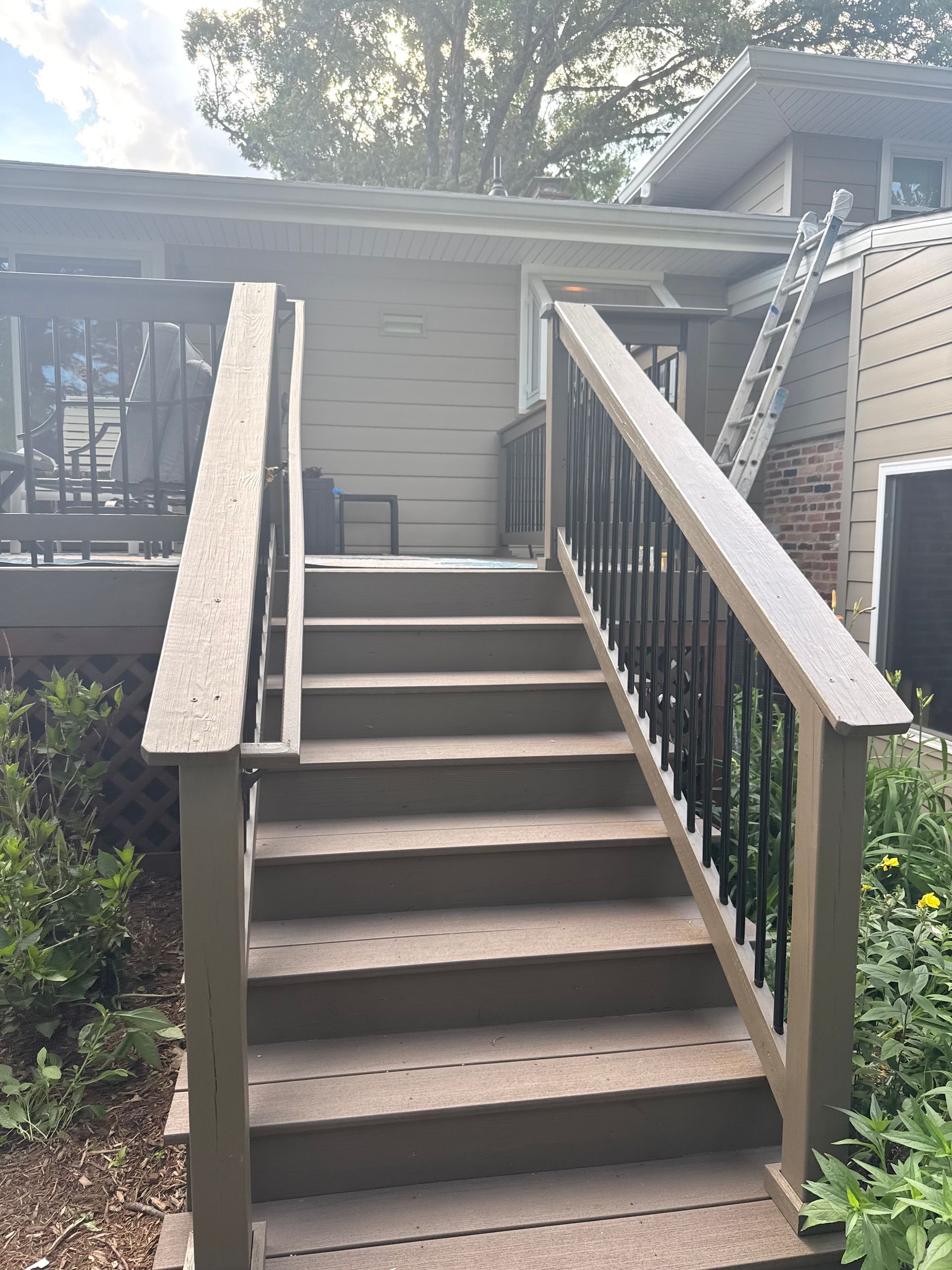 Front steps with concrete stairs and black metal railings leading up to a house porch.