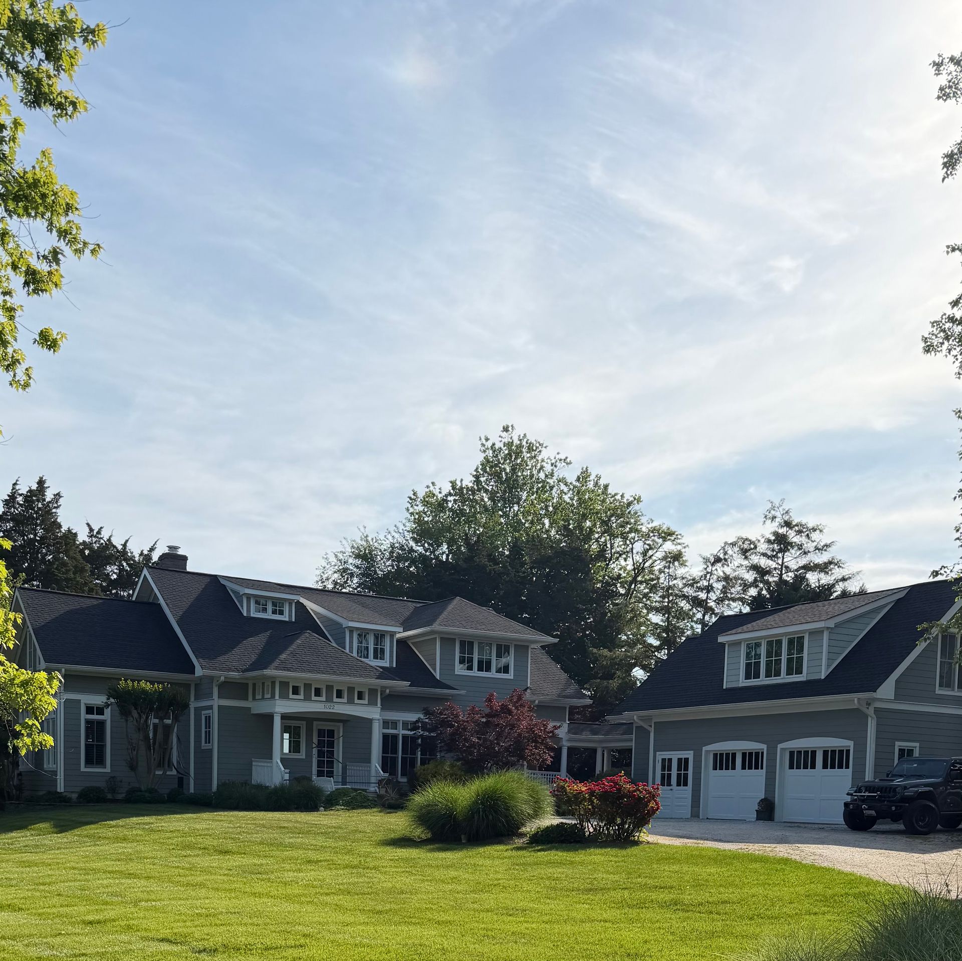 Two-story suburban house with a gray roof, green lawn, and trees under a bright sky