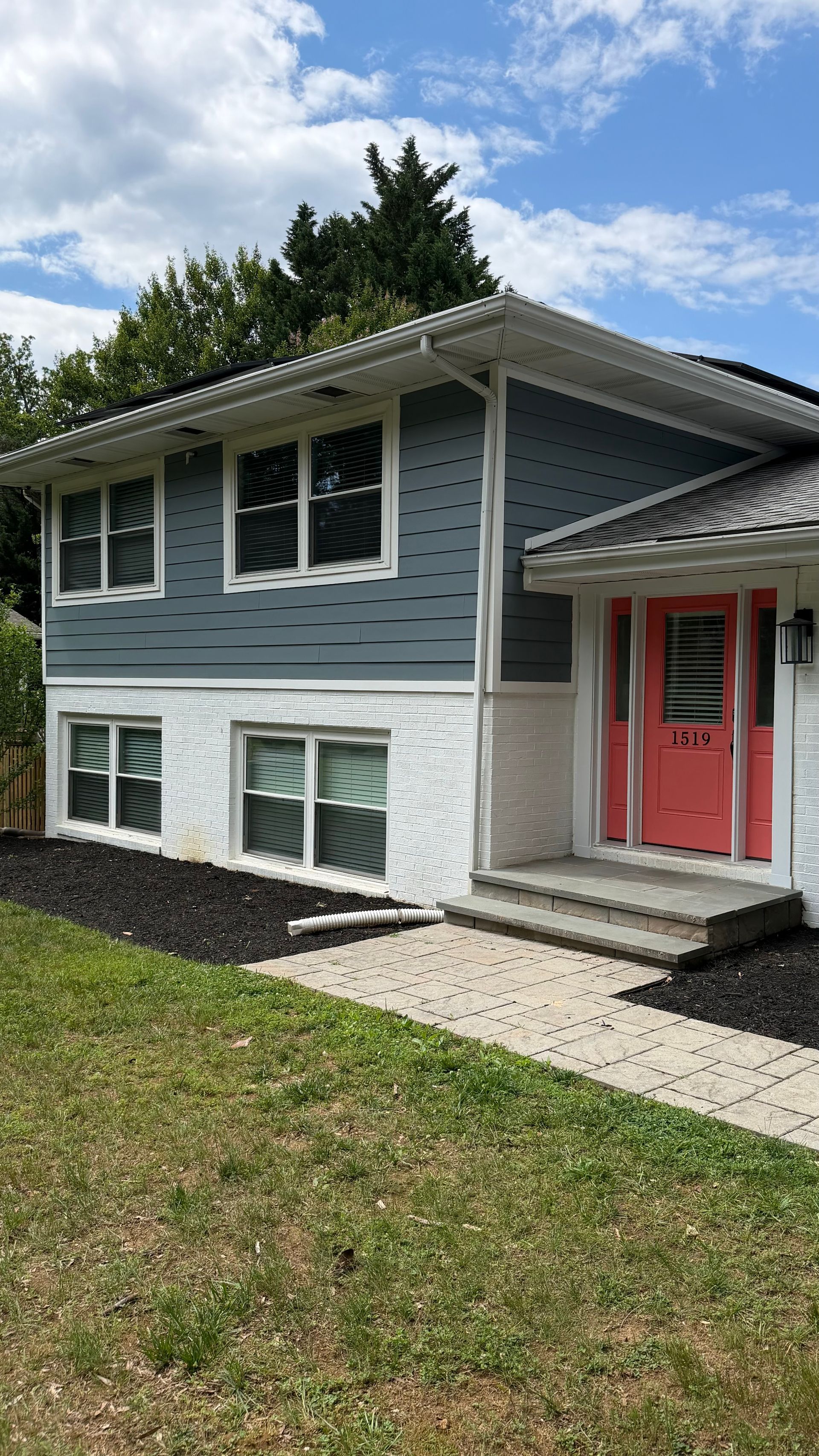 Blue split-level house with white trim, red front door, and a small front lawn under a partly cloudy sky