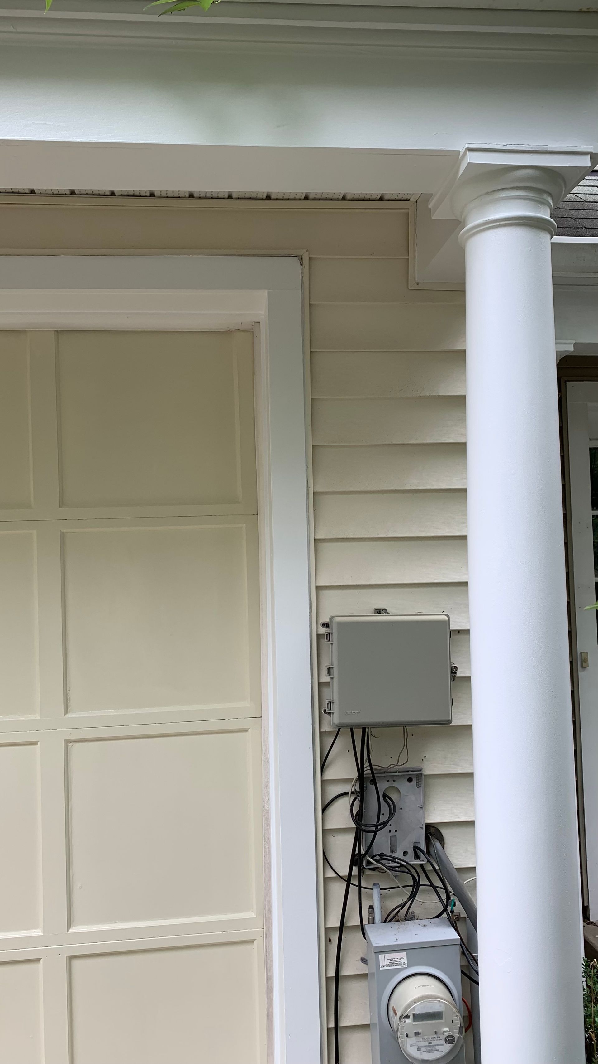 Front porch with white columns, beige siding, door, and utility boxes with exposed wires