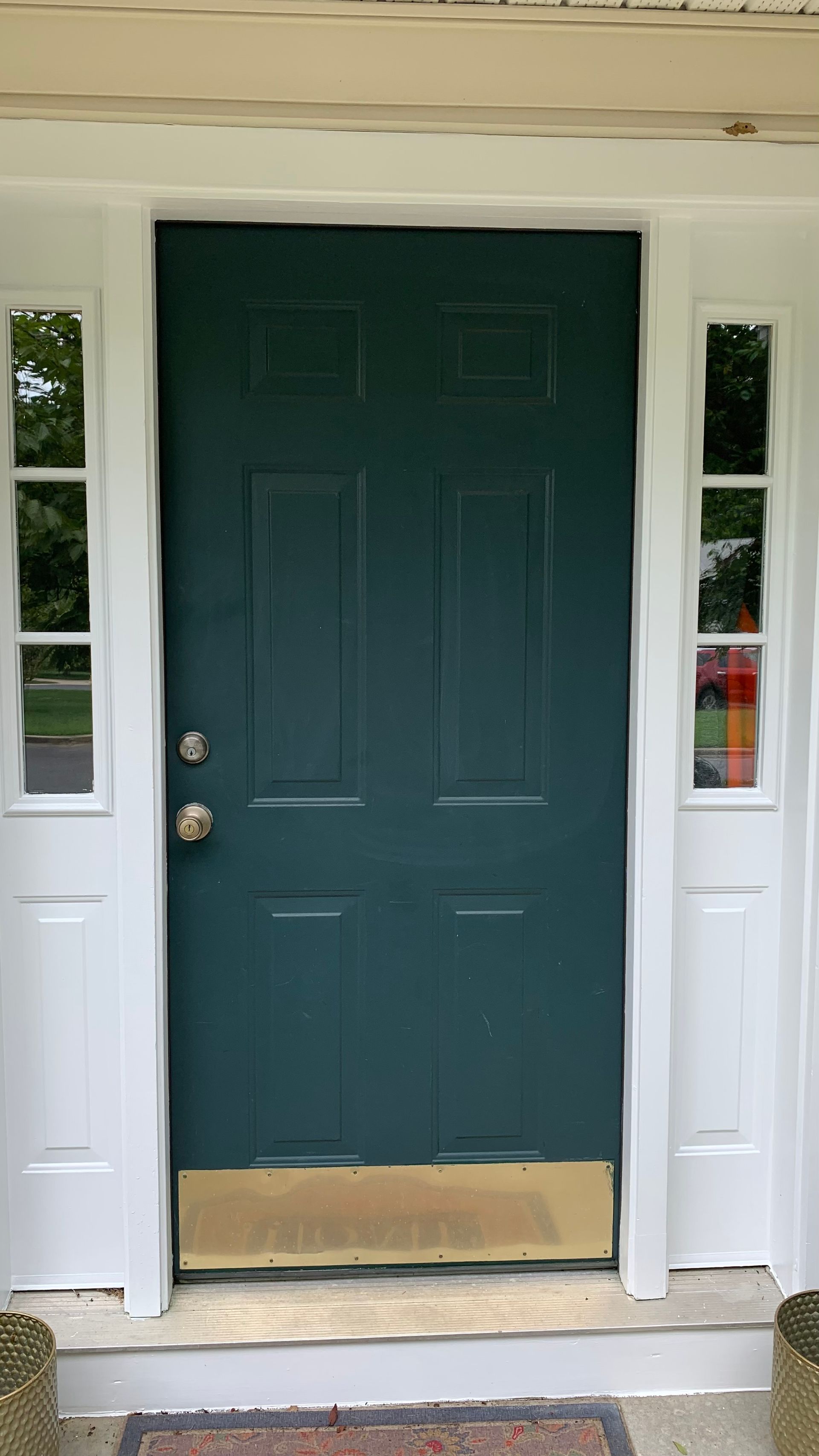 Green front door with sidelights and a tan kick plate on a house porch